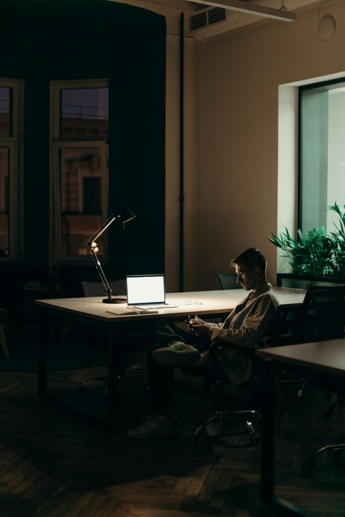 A young man using a laptop at night in a dimly lit office space, focused on his work.